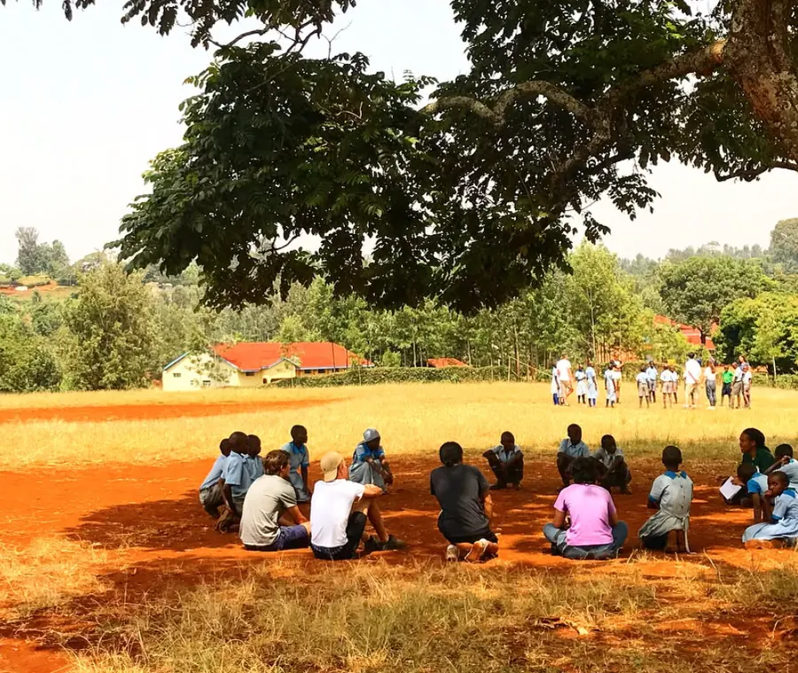 Children sitting outdoors under a tree, supported through educational work with Verdant