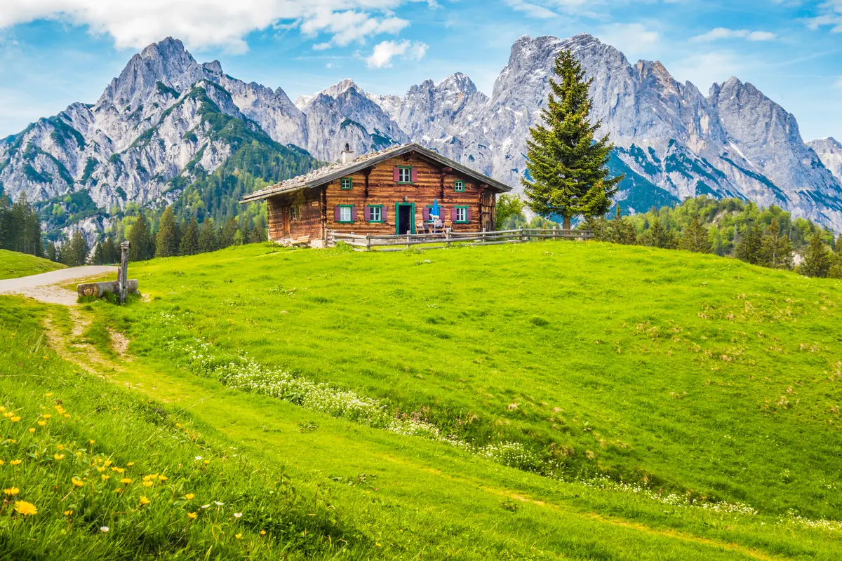 A Swiss chalet on a green meadow below the mountains
